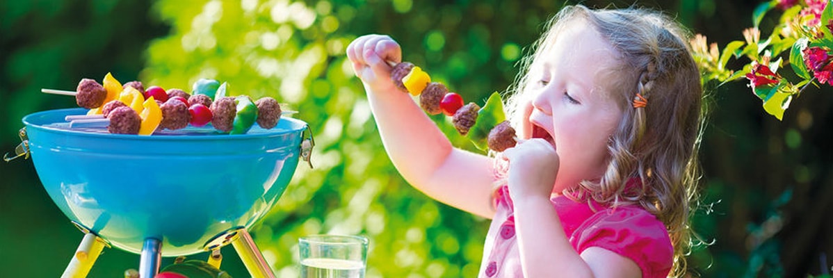 Bambina che mangia spiedini di carne e verdure alla griglia.