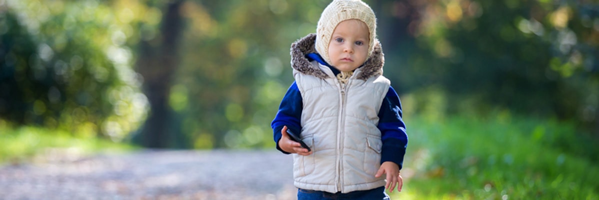 Bambino con giubbotto e cappello che tiene un telefono.