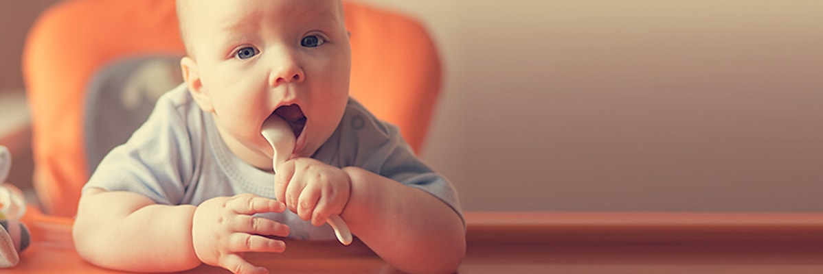 Baby mit Löffel im Hochstuhl.