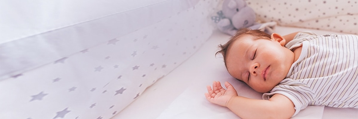Baby schläft in einem Bettchen in gestreiften Kleidern.