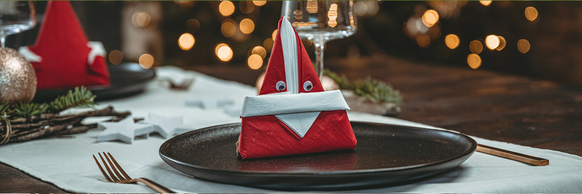 Tovaglioli a forma di Babbo Natale su piatti neri, tavola natalizia.