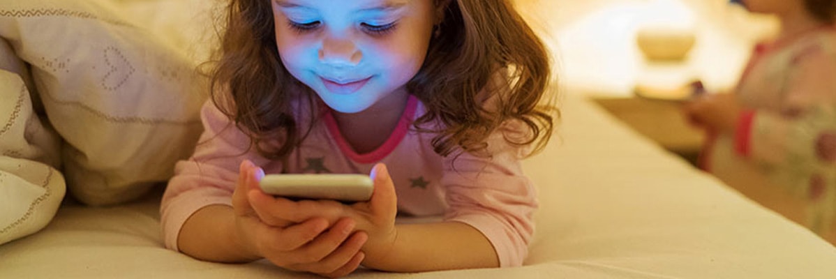 Bambina che usa uno smartphone a letto.
