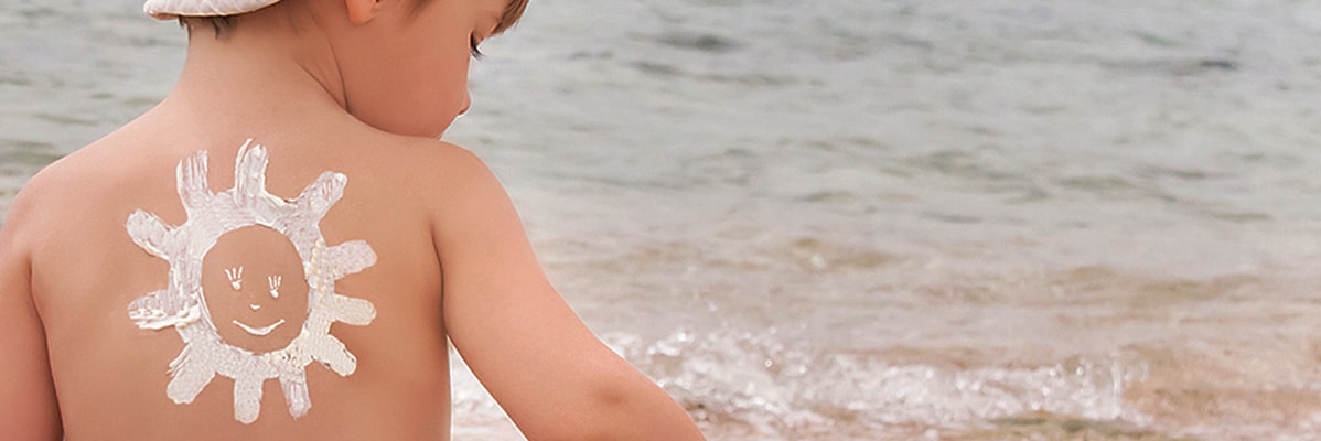 Bambino in spiaggia con crema solare a forma di sole.