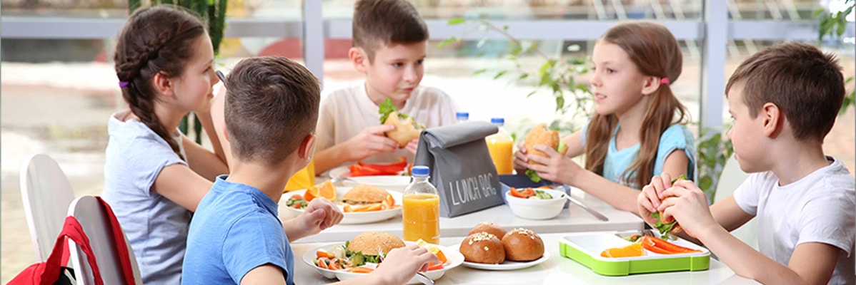 Bambini che mangiano panini e frutta a scuola.