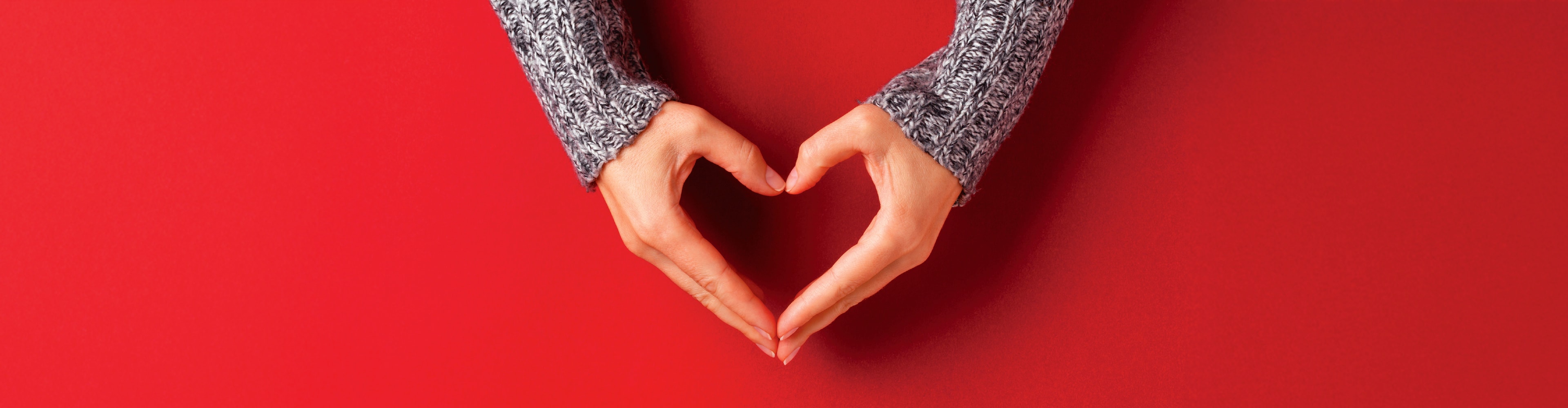 Hände formen ein Herz auf rotem Hintergrund.