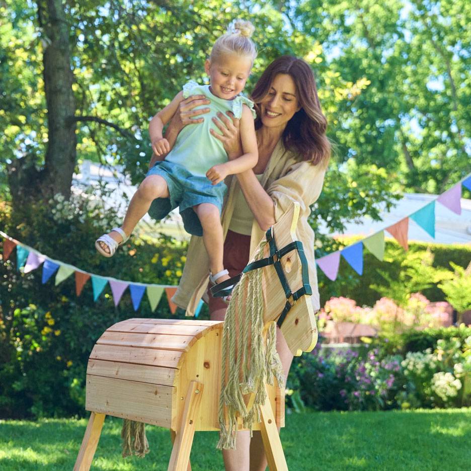 Femme et enfant avec un cheval à bascule en bois dans un jardin décoré.