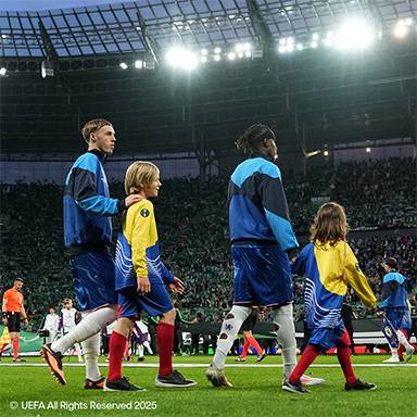 Fußballspieler und Kinder in blauen und gelben Trikots betreten ein Stadionfeld.