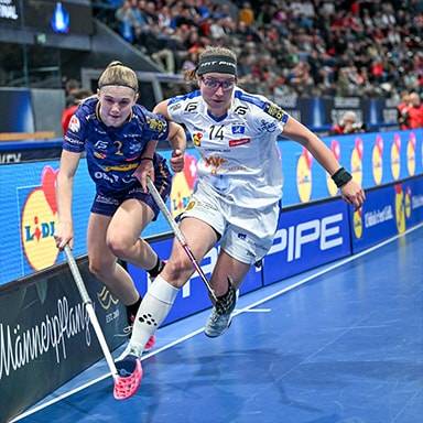 Due donne giocano a floorball in un'arena con cartelloni pubblicitari Pipe e Lidl.