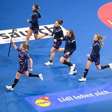 Donne che corrono su un campo da pallamano blu con il logo Lidl.
