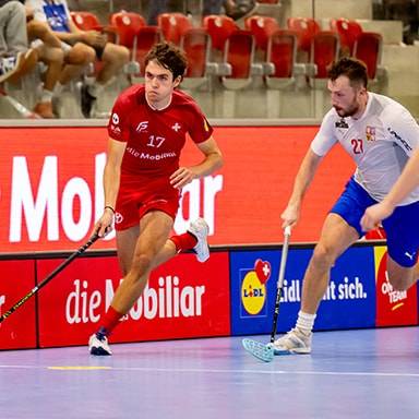 Due giocatori di floorball in azione su un campo, con uno che dribbla e l'altro che difende.