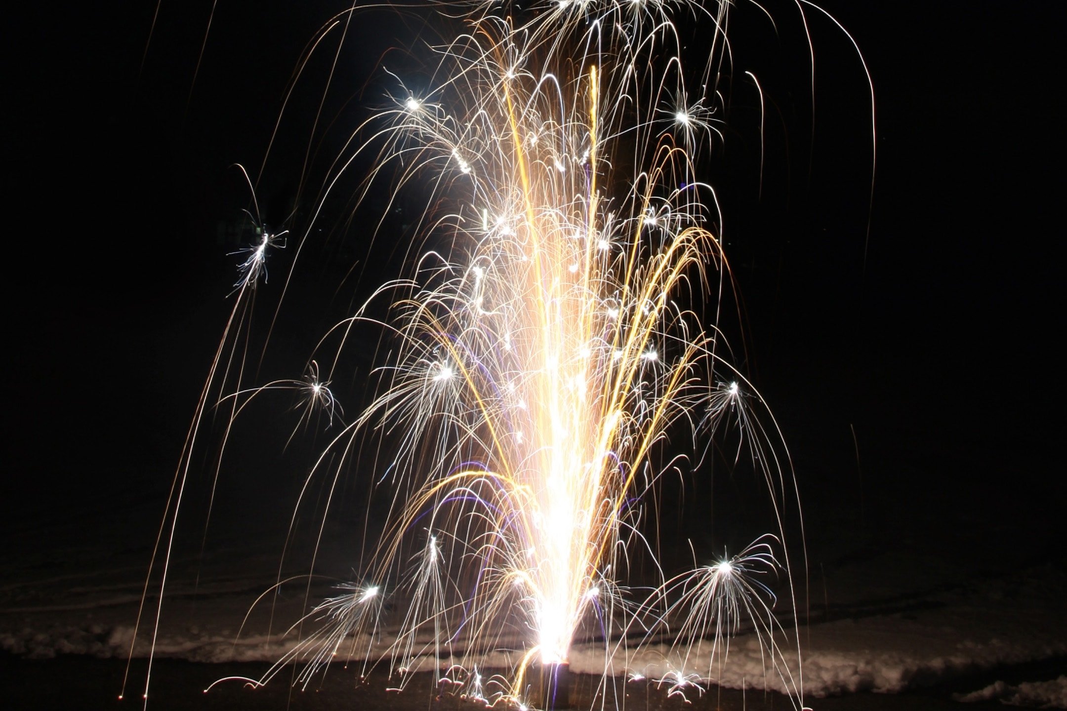 Leuchtendes Feuerwerk in der dunklen Nacht, mit goldenen und weißen Funken.