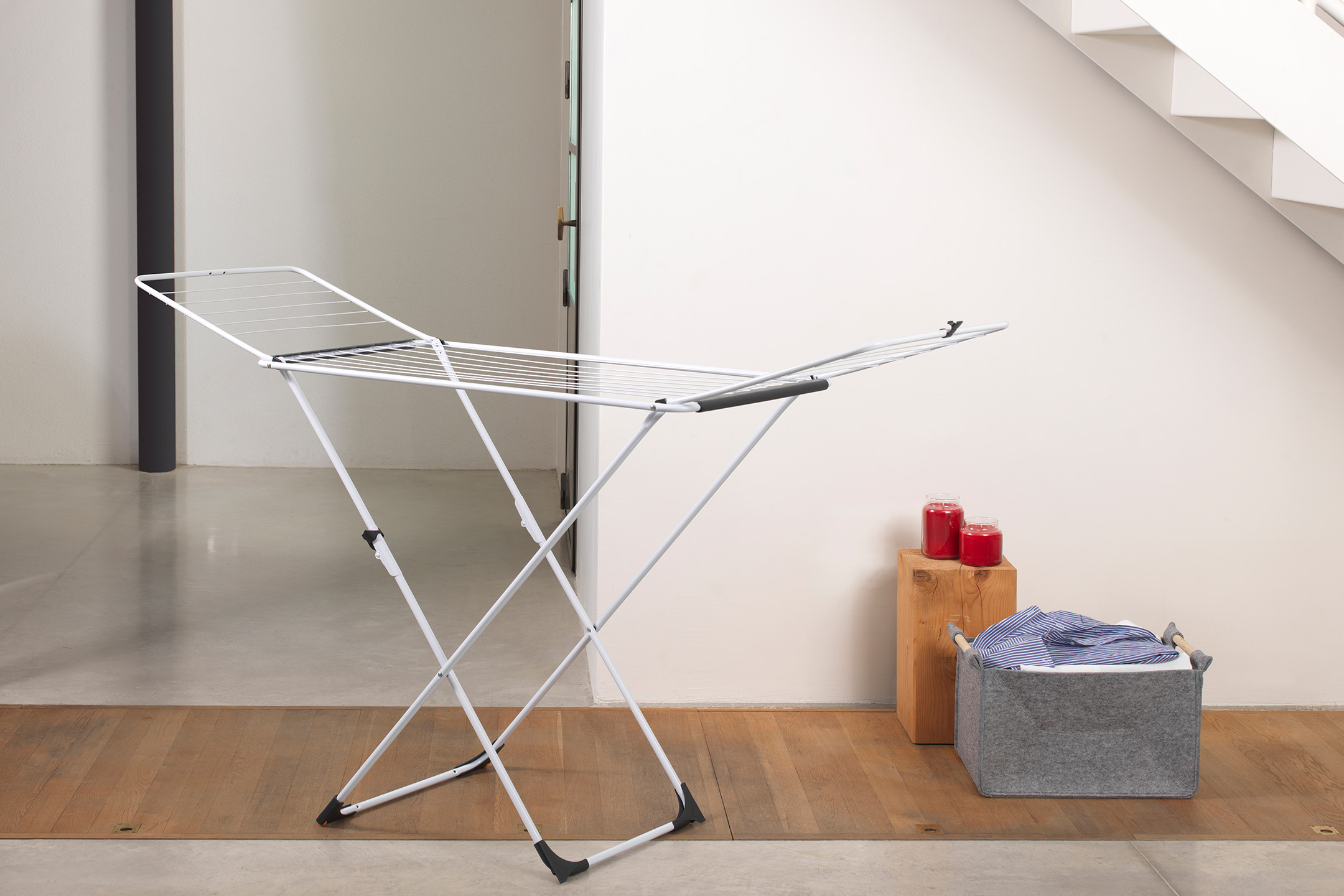 Weißer klappbarer Wäscheständer mit einem Wäschekorb und roten Kerzen.