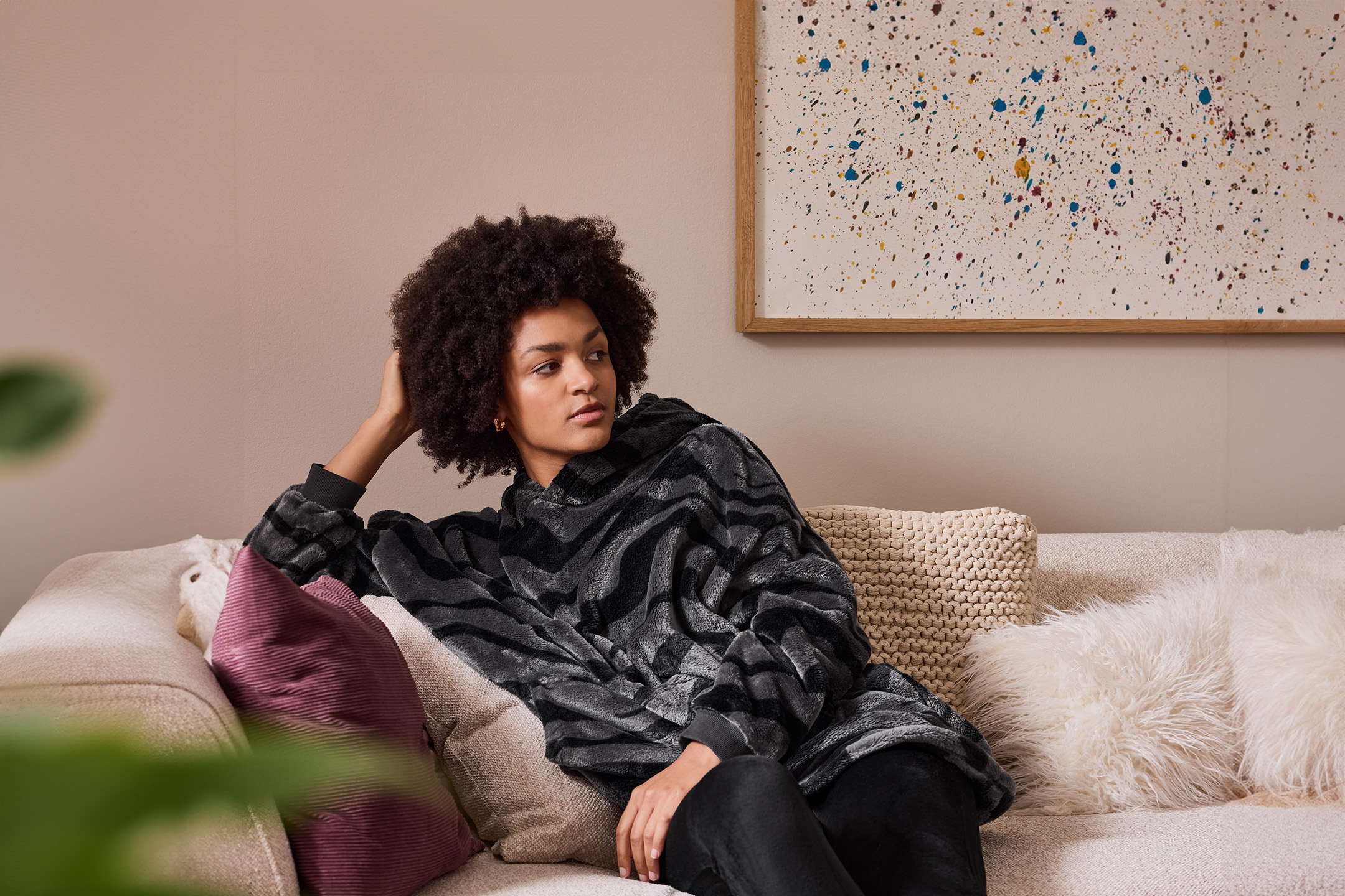 Frau auf einem Sofa, die eine graue Kapuzendecke mit Zebramuster trägt.