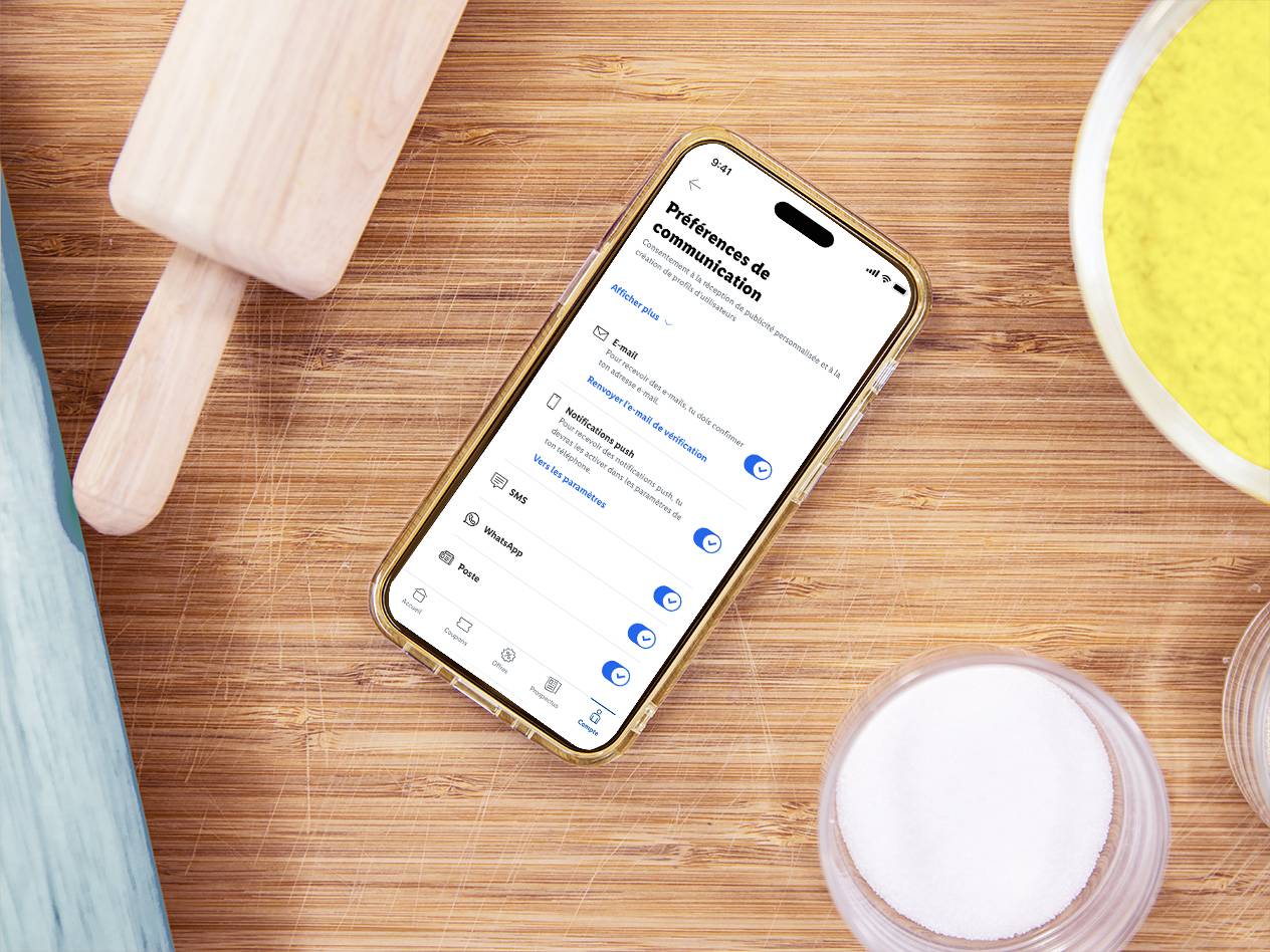 Un smartphone affichant les préférences de communication sur une table en bois avec des ingrédients de cuisine.