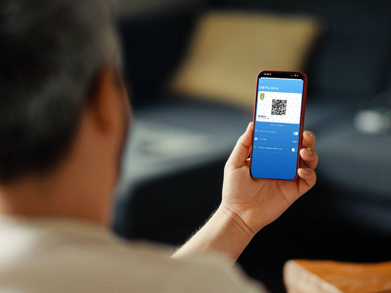 Ein Mann hält ein Smartphone mit einer digitalen Zahlungskarte und einem QR-Code.