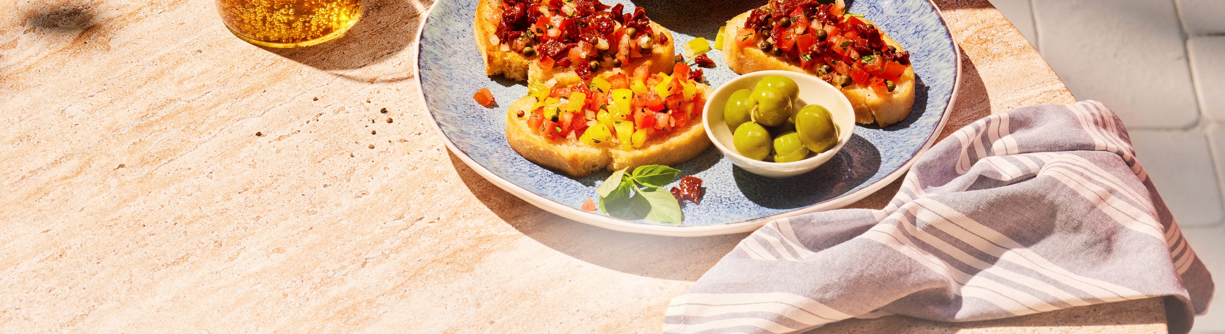 Bruschetta mit Tomaten und Oliven auf einem Steintisch, mit einem Getränk.