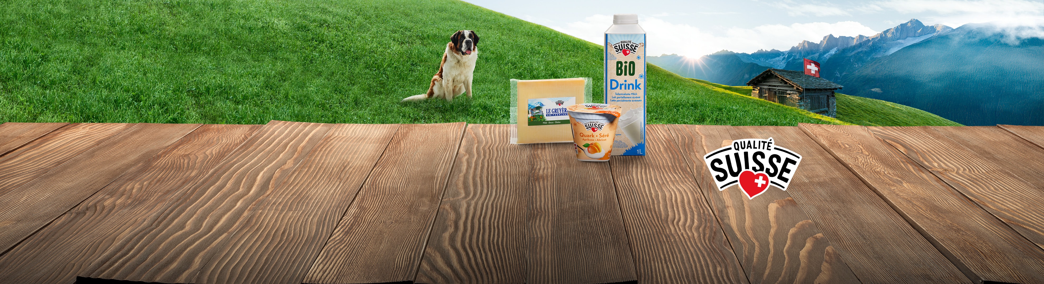 Bevanda biologica, formaggio Le Gruyère e quark all'albicocca su un tavolo di legno con un San Bernardo e uno chalet svizzero sullo sfondo.