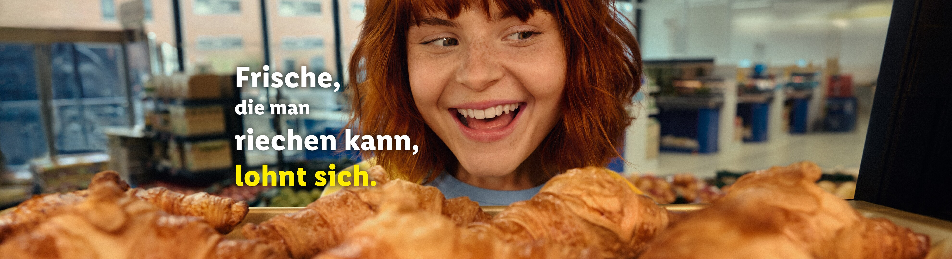 Eine lächelnde Frau blickt auf frische Croissants mit dem Text „Frische, die man riechen kann, lohnt sich“.