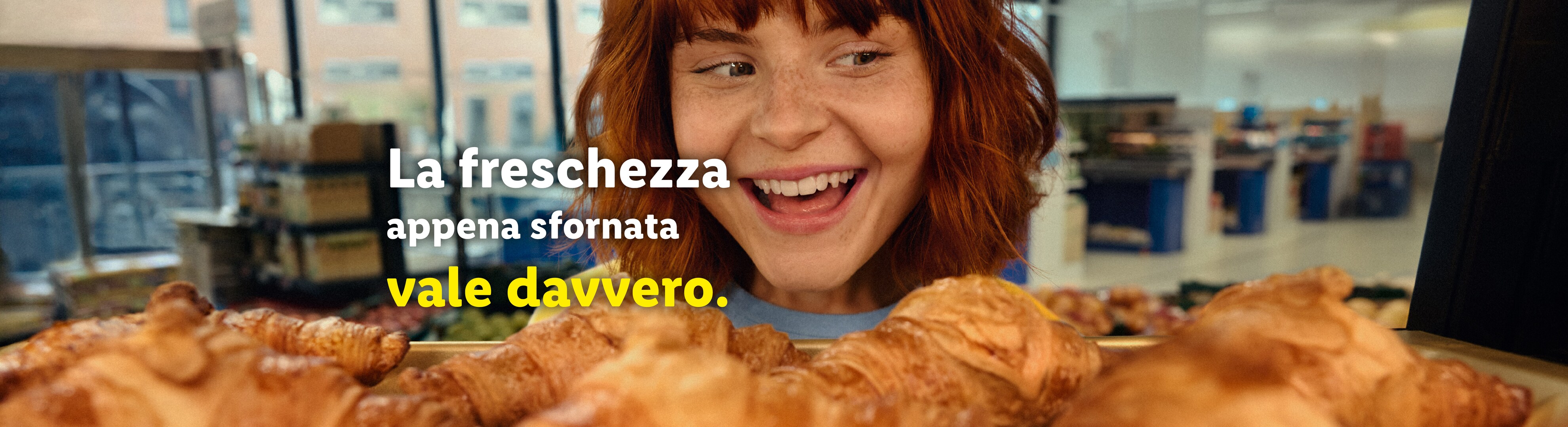 Una donna sorridente guarda dei croissant appena sfornati con il testo 'La freschezza appena sfornata vale davvero'.