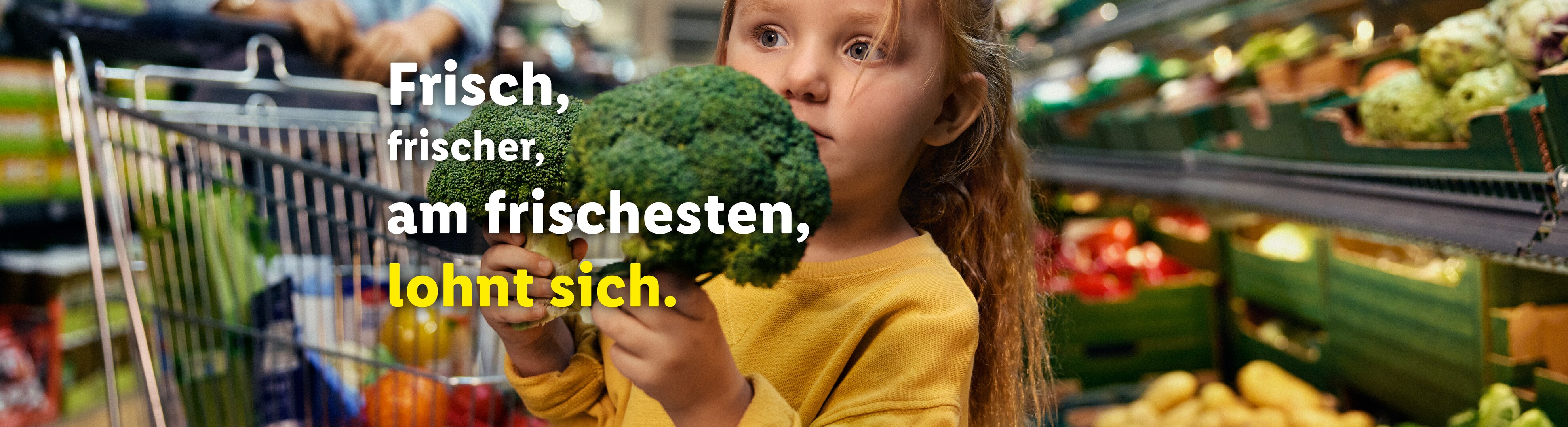 Ein kleines Mädchen hält frischen Brokkoli in einem Supermarkt.
