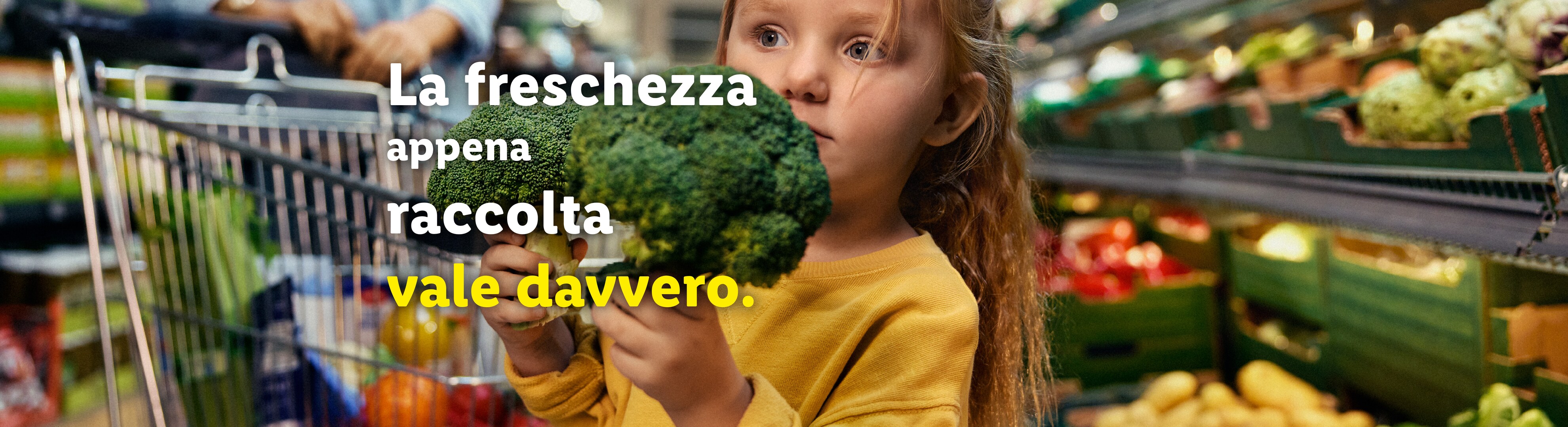 Bambina con broccoli freschi in un supermercato.