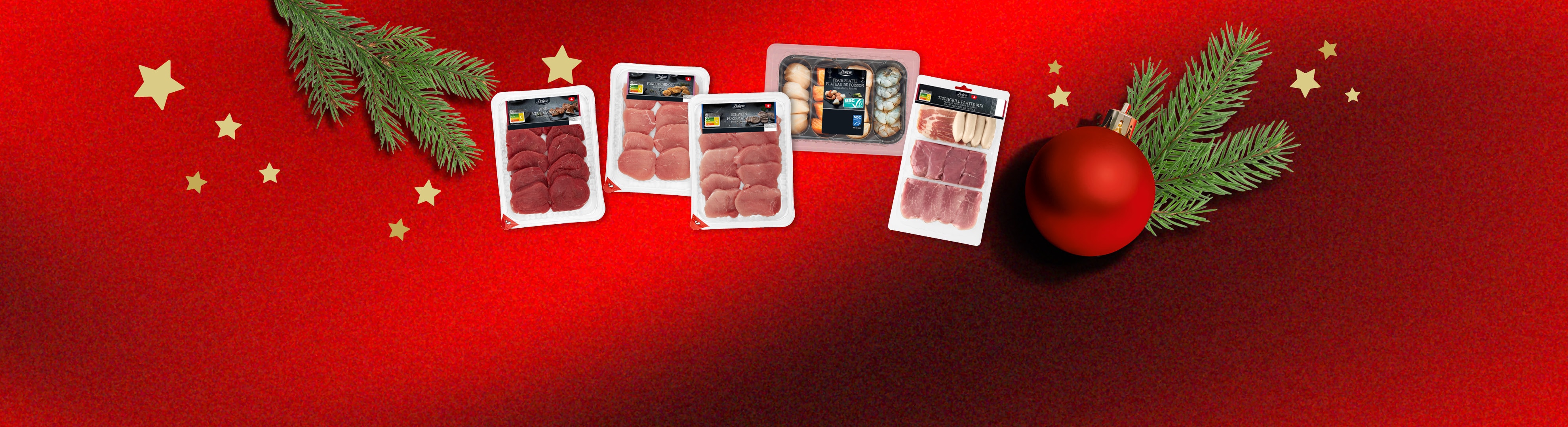 Deluxe Fleisch- und Fischauswahl für die Feiertage auf rotem Hintergrund mit Weihnachtsdeko.