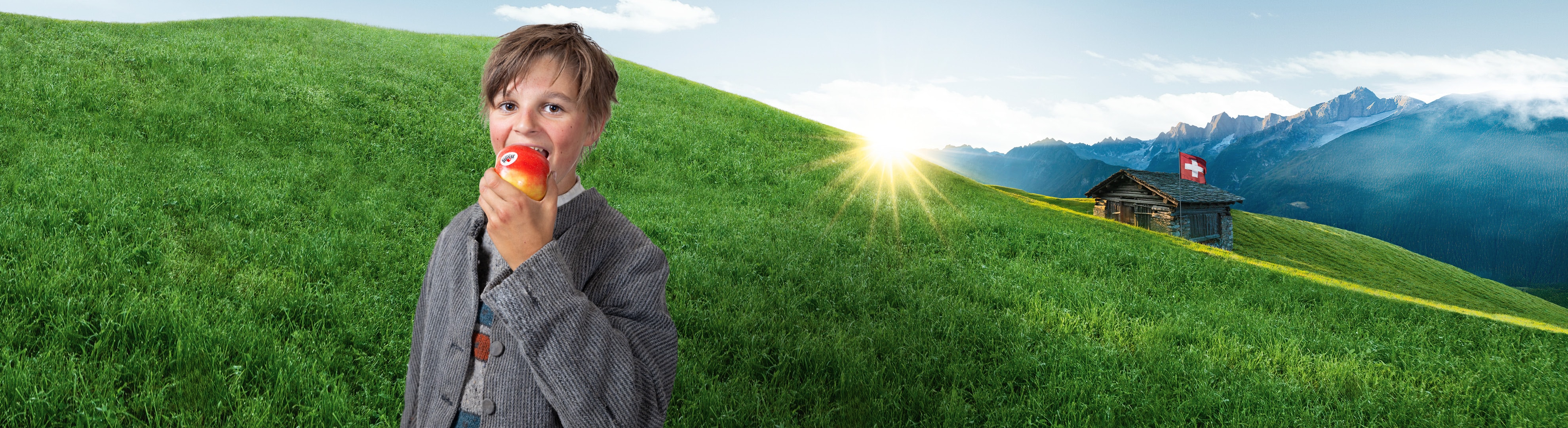 Ein Kind isst einen Apfel in einer Alpenlandschaft mit einer Schweizer Hütte.