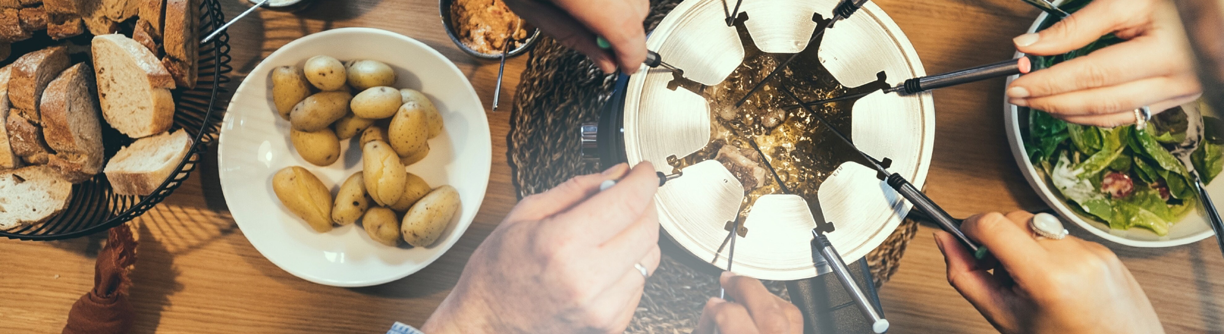 Personen essen Fleischfondue mit Brot, Kartoffeln und Salat.