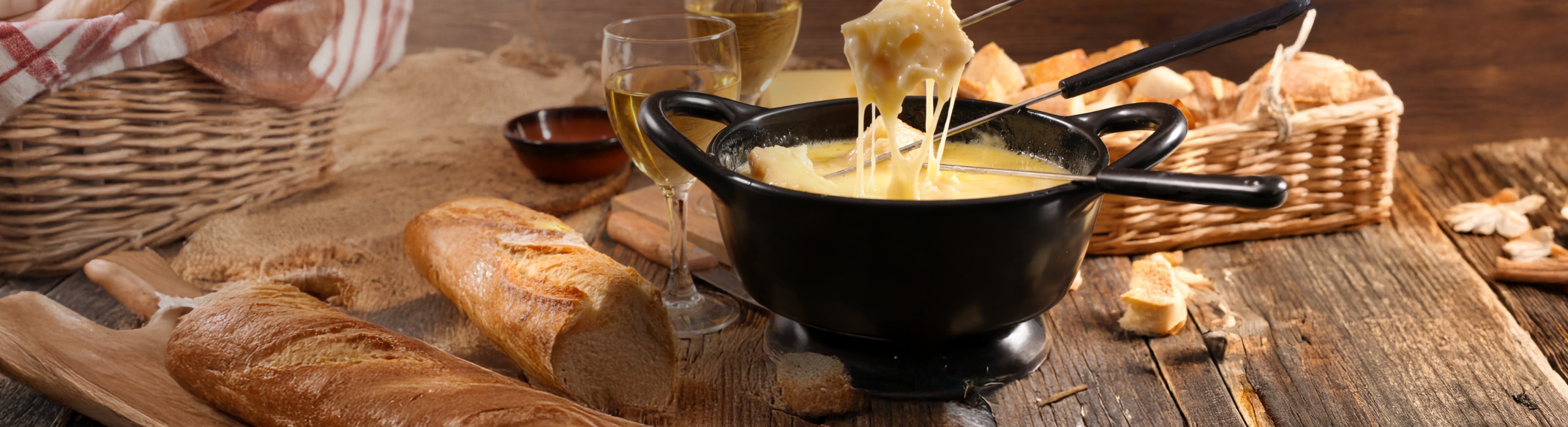 Käsefondue mit Brot und Weißwein auf einem Holztisch.