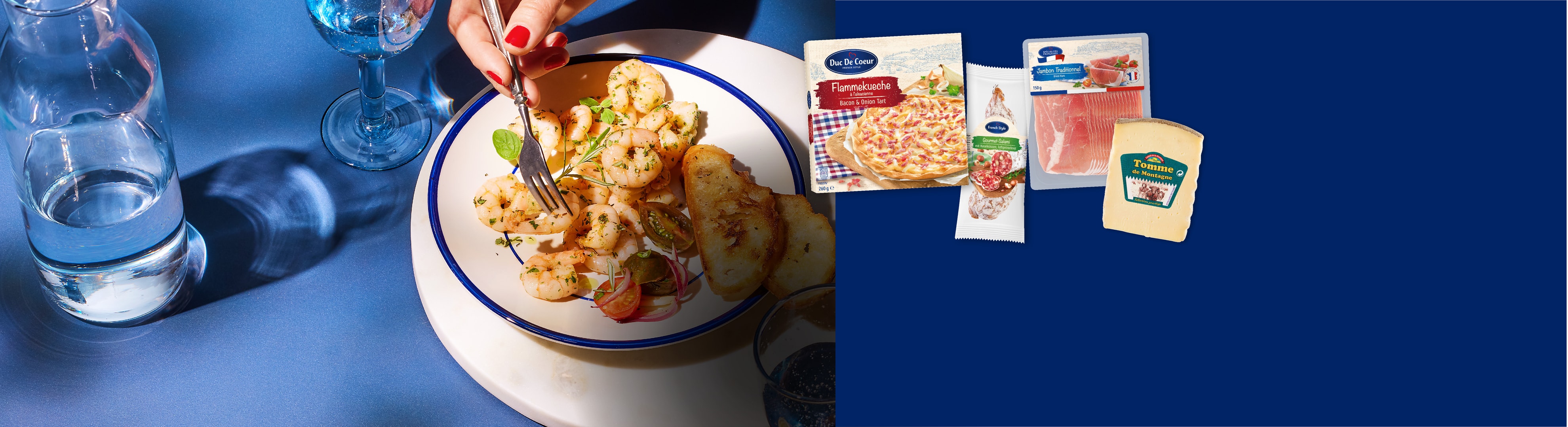 Eine Person isst Garnelen und Toastbrot, mit Flammkuchen, Wurstwaren und Käse im Hintergrund.