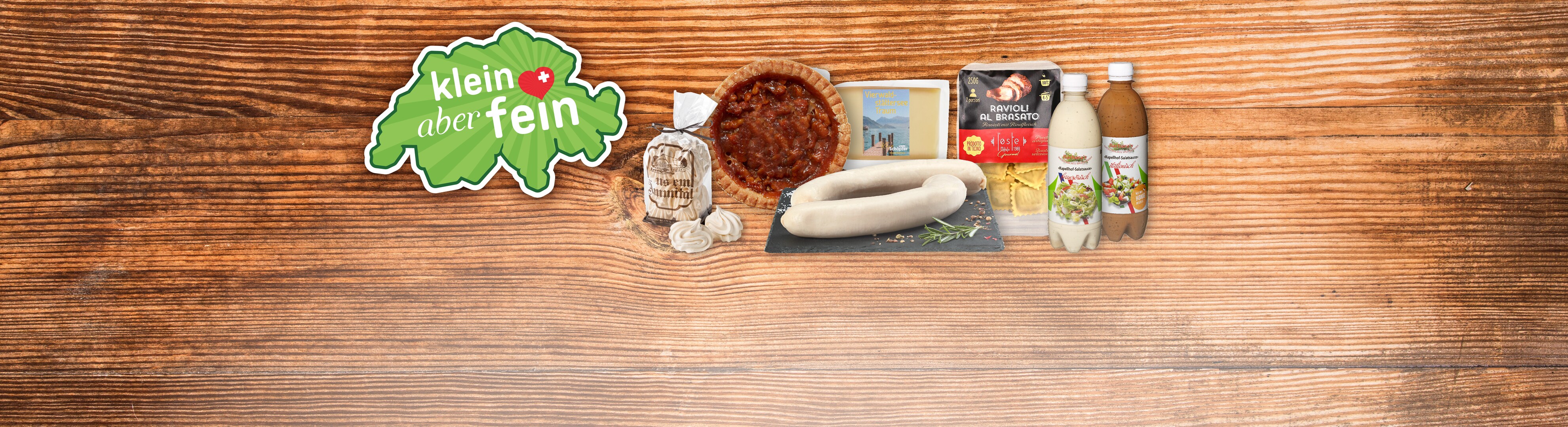 Eine Auswahl an Schweizer Lebensmitteln, darunter Ravioli, Meringues und Saucen, auf einem Holztisch.