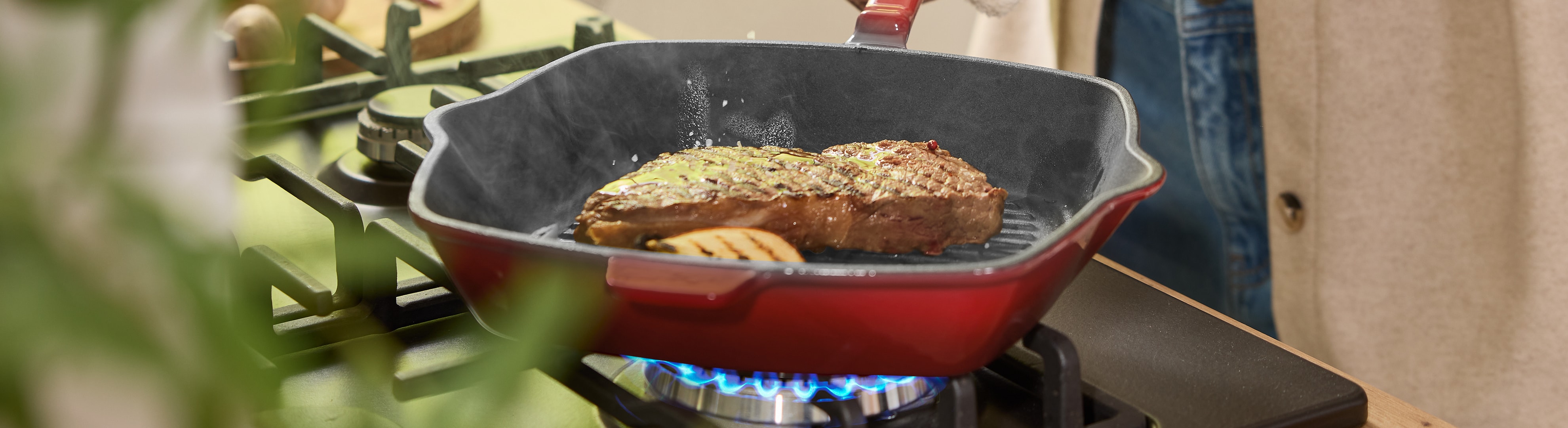 Steak brutzelt in einer roten Pfanne auf einem Gasherd.