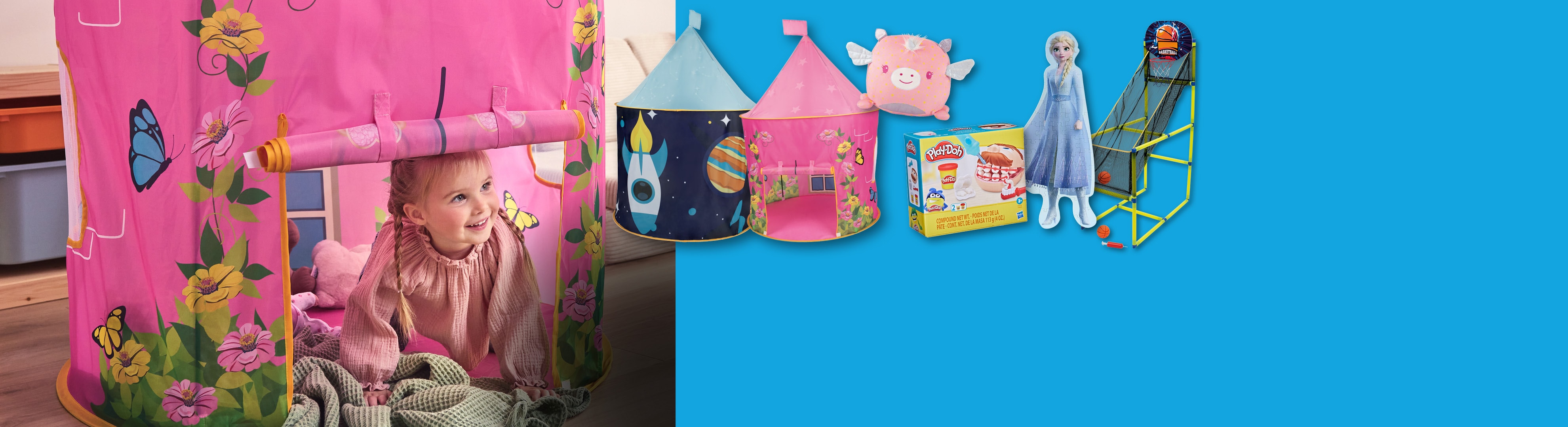 Une petite fille joue dans une tente rose à motifs floraux, avec d'autres jouets à côté.