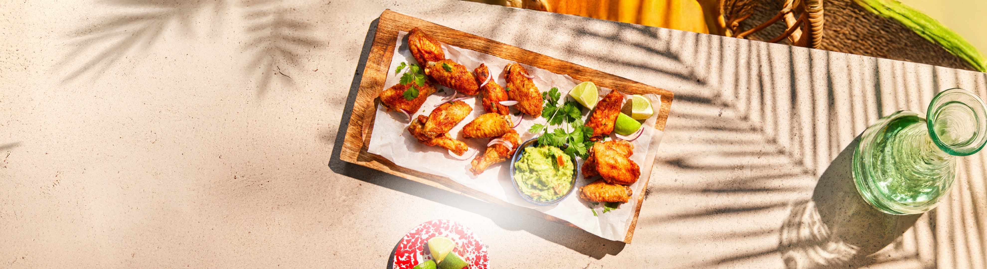 Gebratene Hähnchenflügel mit Guacamole und Limetten auf einem Betontisch.