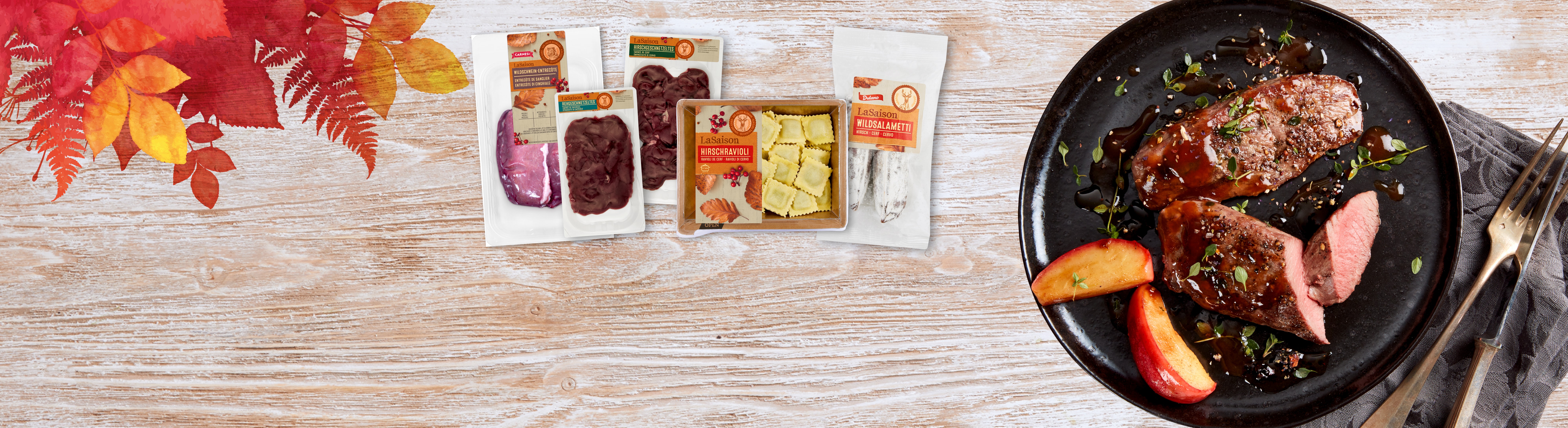 Verpacktes Wildfleisch und Ravioli, mit einem Teller gekochtem Fleisch und Äpfeln auf einem Holztisch.