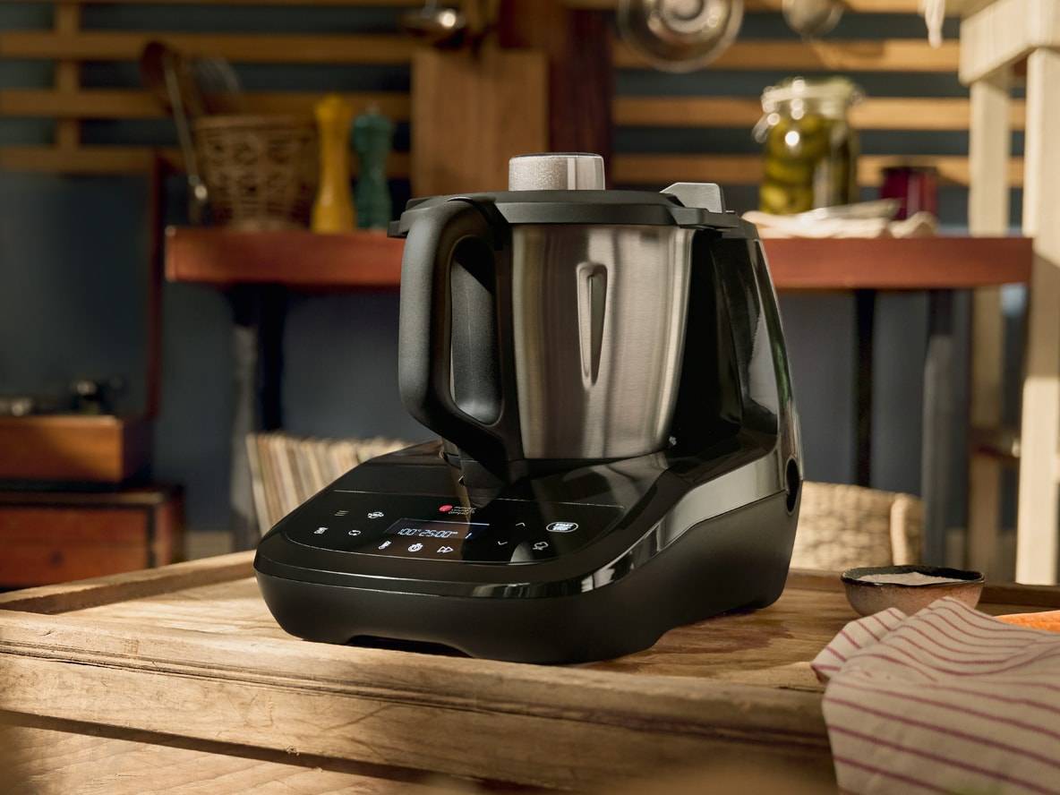 Schwarze und silberne Multifunktions-Küchenmaschine auf einem Holztisch in einer rustikalen Küche.