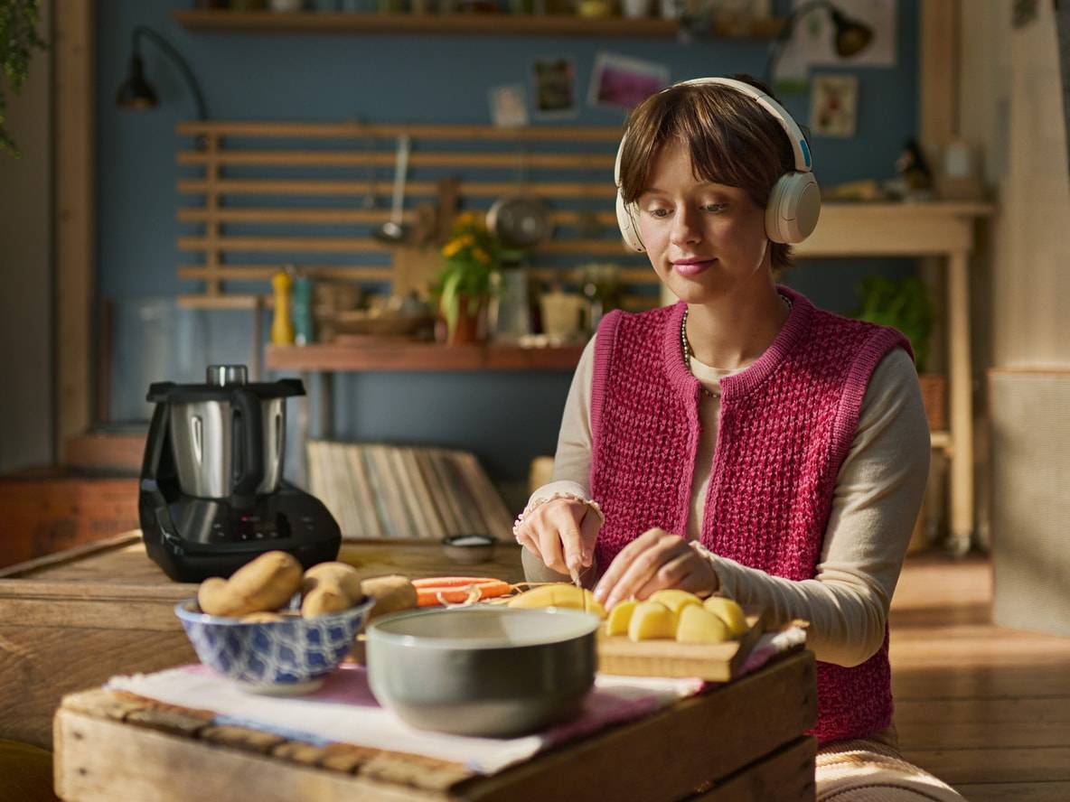 Frau mit Kopfhörern schneidet Gemüse, ein Silvercrest Monsieur Cuisine Smart auf dem Tisch.