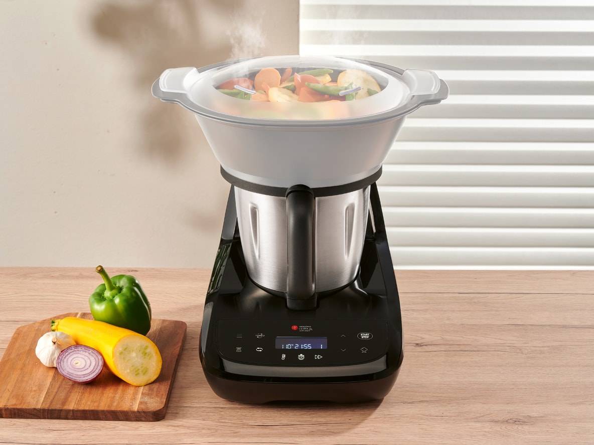 Multifunktions-Küchenmaschine mit Dampfgarer, frisches Gemüse auf einem Schneidebrett.