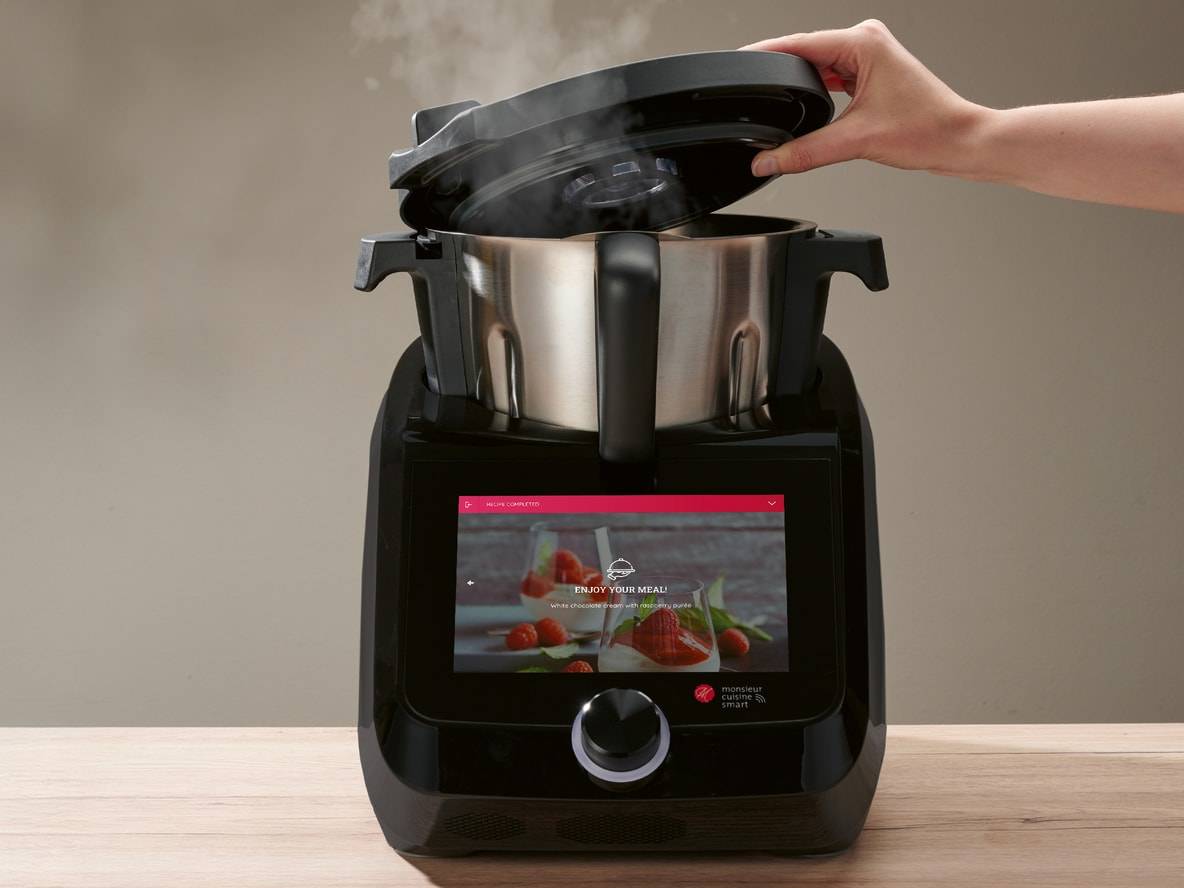 Schwarze Monsieur Cuisine Smart Küchenmaschine mit angehobenem Deckel und Dampf, Rezept auf dem Display.