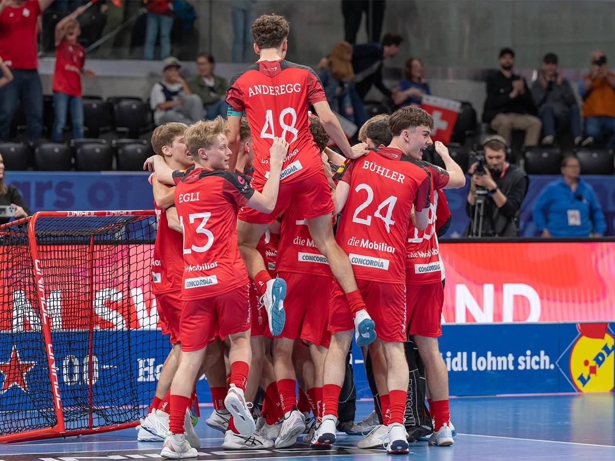 Giocatori di floorball in maglie rosse con sponsorizzazioni come Concordia e Lidl, che si abbracciano in campo.