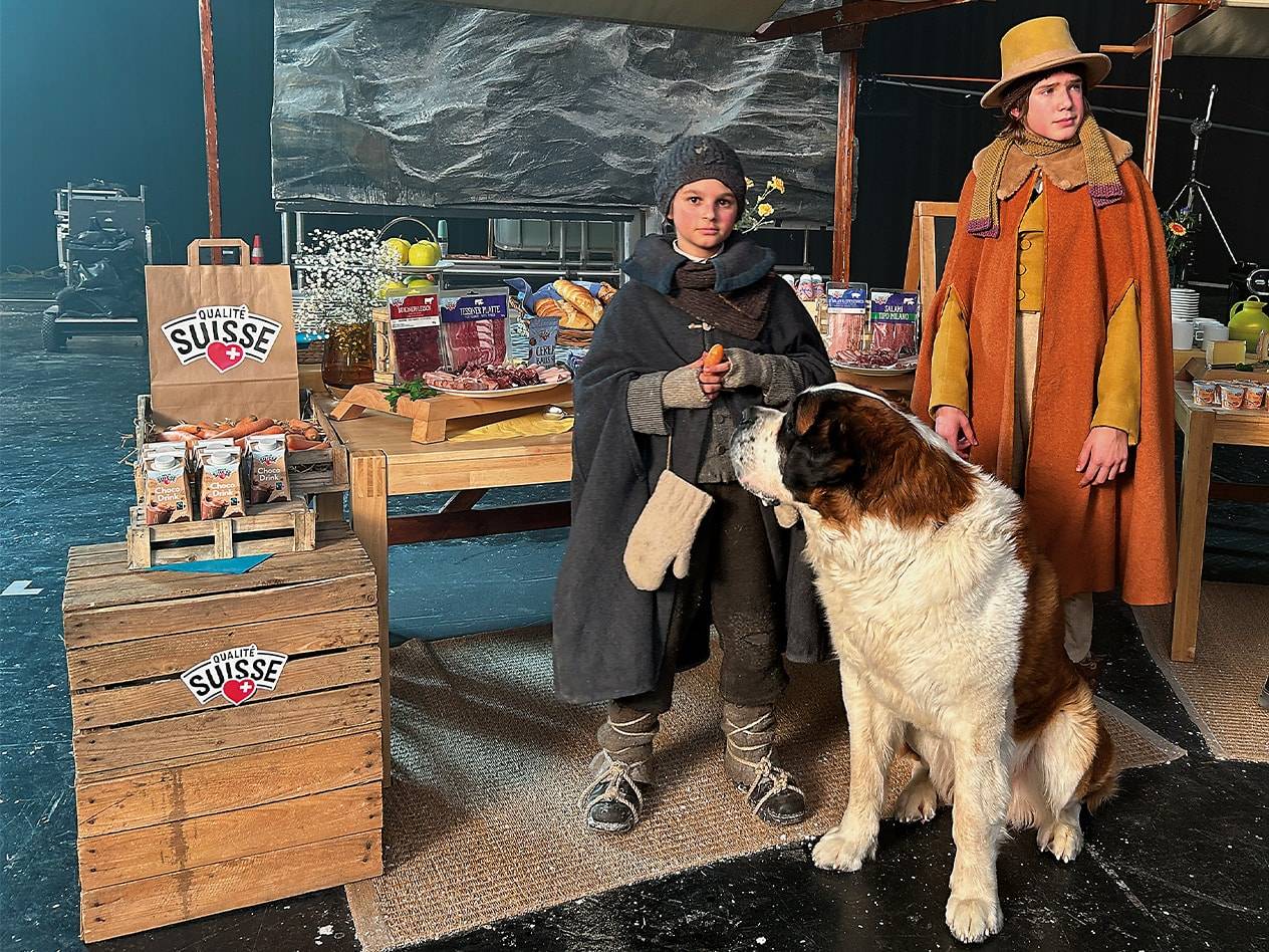 Kinder in historischen Kostümen mit Bernhardiner, Qualité Suisse Produkten und Wurstwaren.