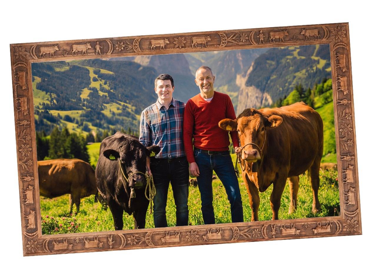 Due uomini con mucche su un prato di montagna, incorniciati da una cornice in legno intagliato.
