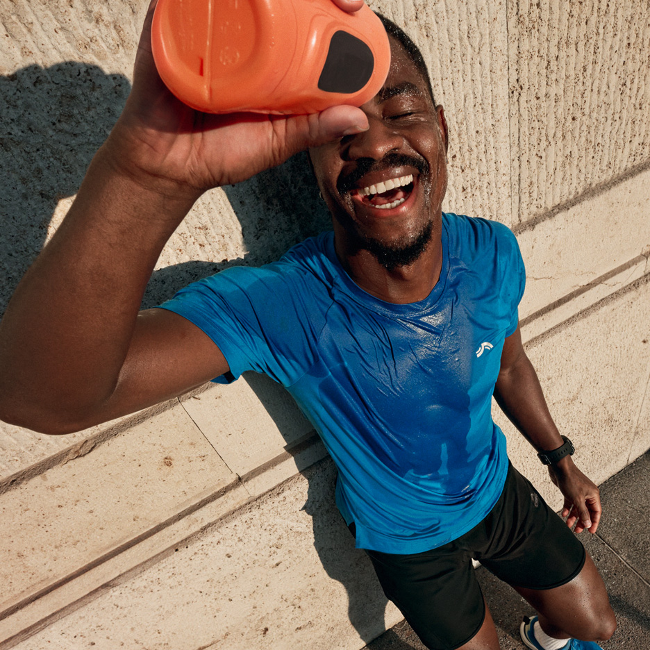 Homme en t-shirt de sport bleu et short noir s'arrosant d'eau après l'entraînement.