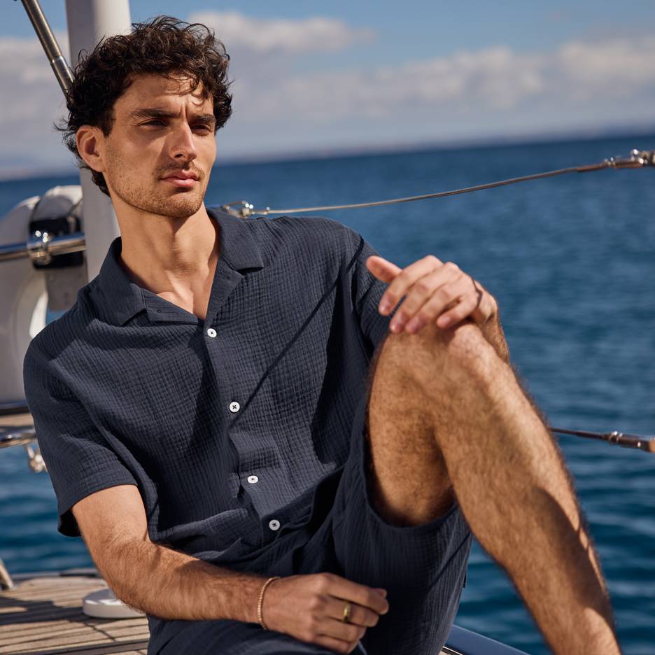 Homme en chemise et short bleu foncé sur un yacht, regardant la mer.