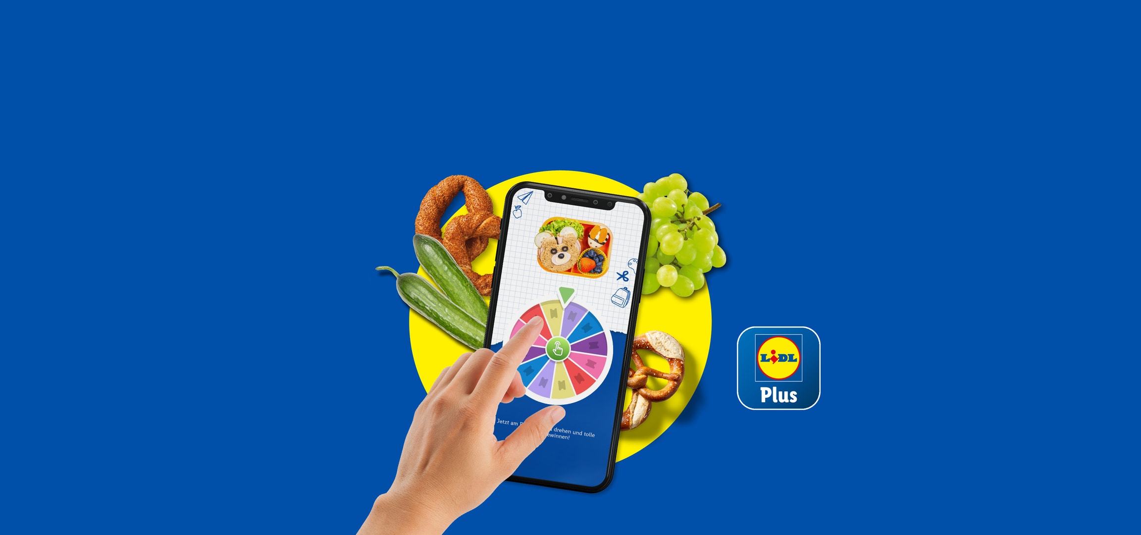 Eine Hand benutzt die Lidl Plus App auf einem Smartphone, mit Brezeln, Gurken und Trauben.