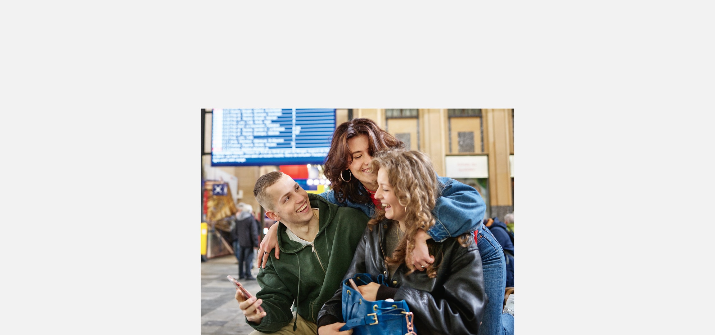 Lachende junge Freunde am Bahnhof, einer hält ein Telefon.