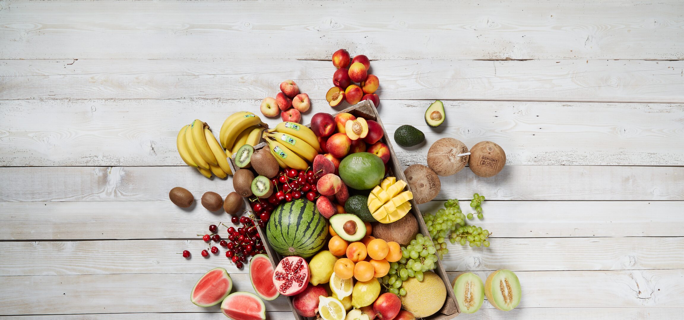 Une caisse en bois pleine de fruits frais et bio, notamment des bananes, des melons, des pommes et des avocats.