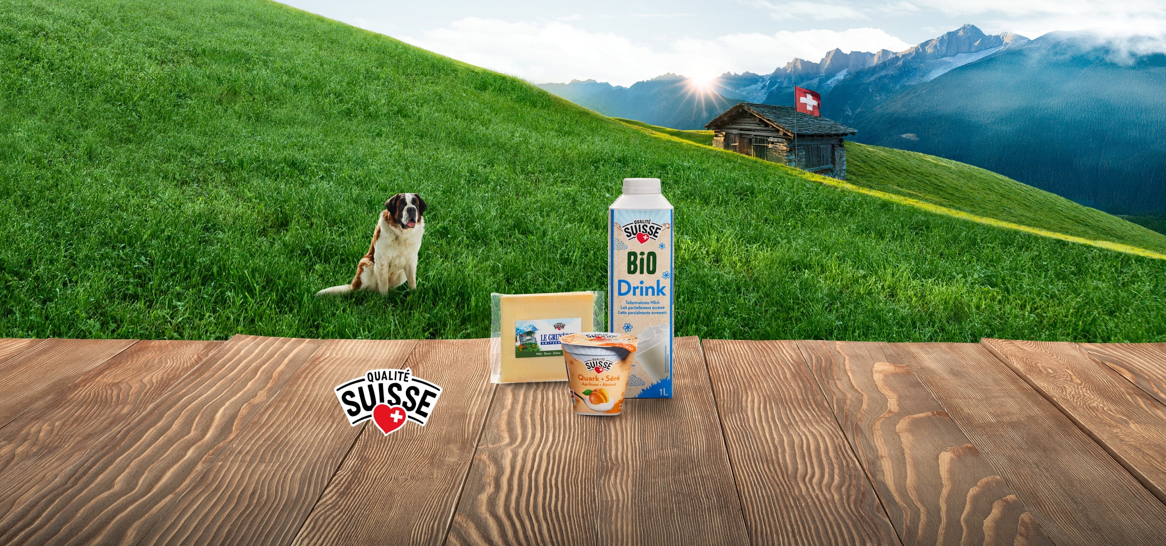Prodotti lattiero-caseari di qualità svizzera su un tavolo di legno con sfondo montano e un cane.