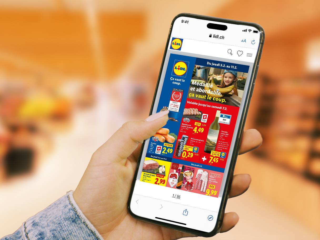 Main tenant un smartphone affichant une brochure numérique avec de la viande, du vin et des vêtements.