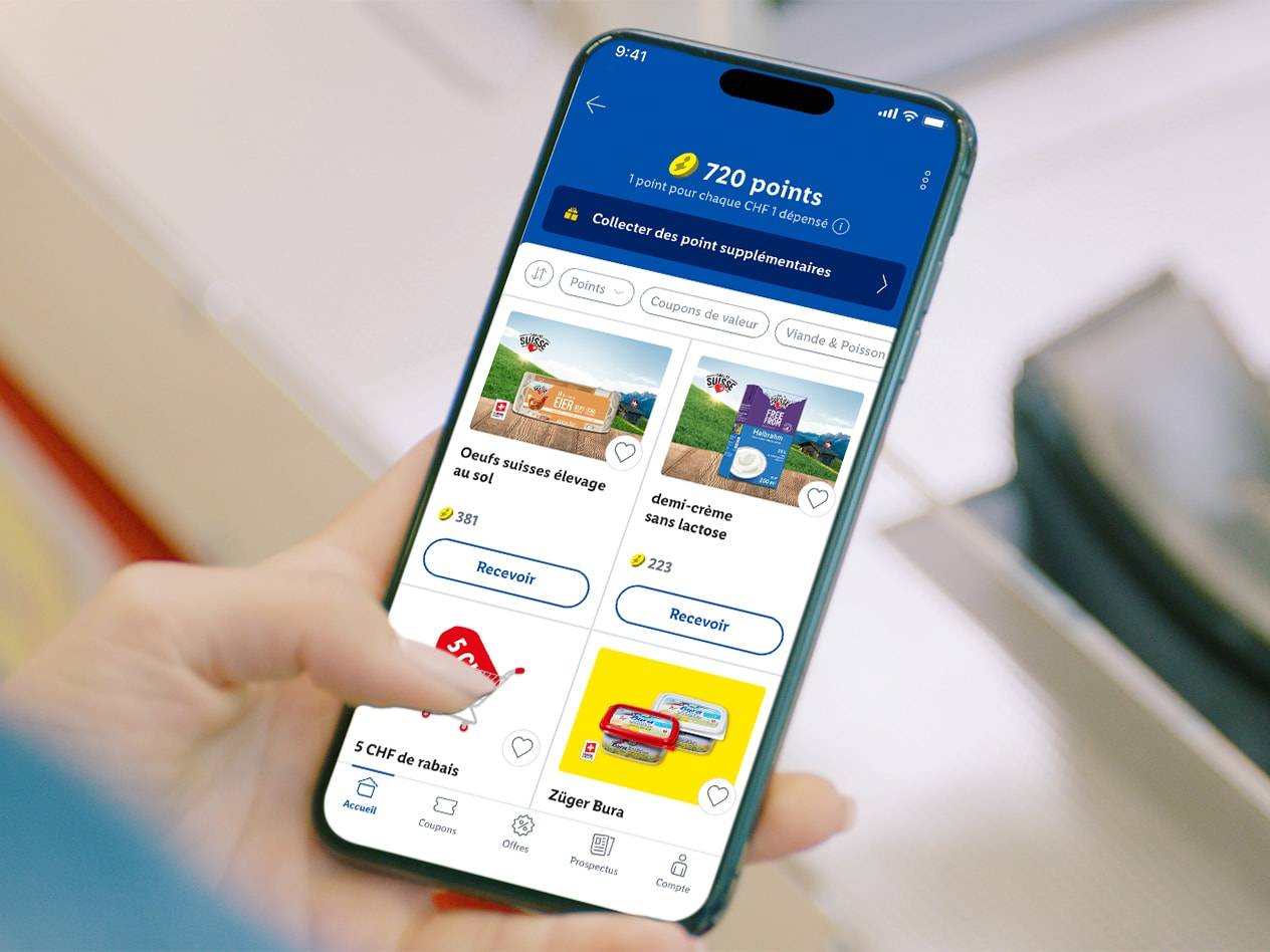 Main tenant un smartphone avec une application affichant des points, des réductions et des produits comme des œufs, de la crème sans lactose et du fromage.